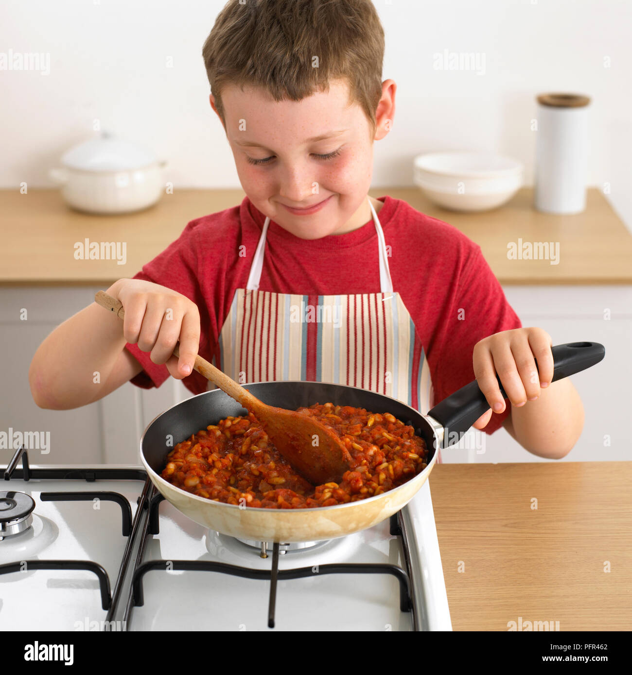 Boy cocinar mezcla de frijoles en la sartén, 8 años Foto de stock