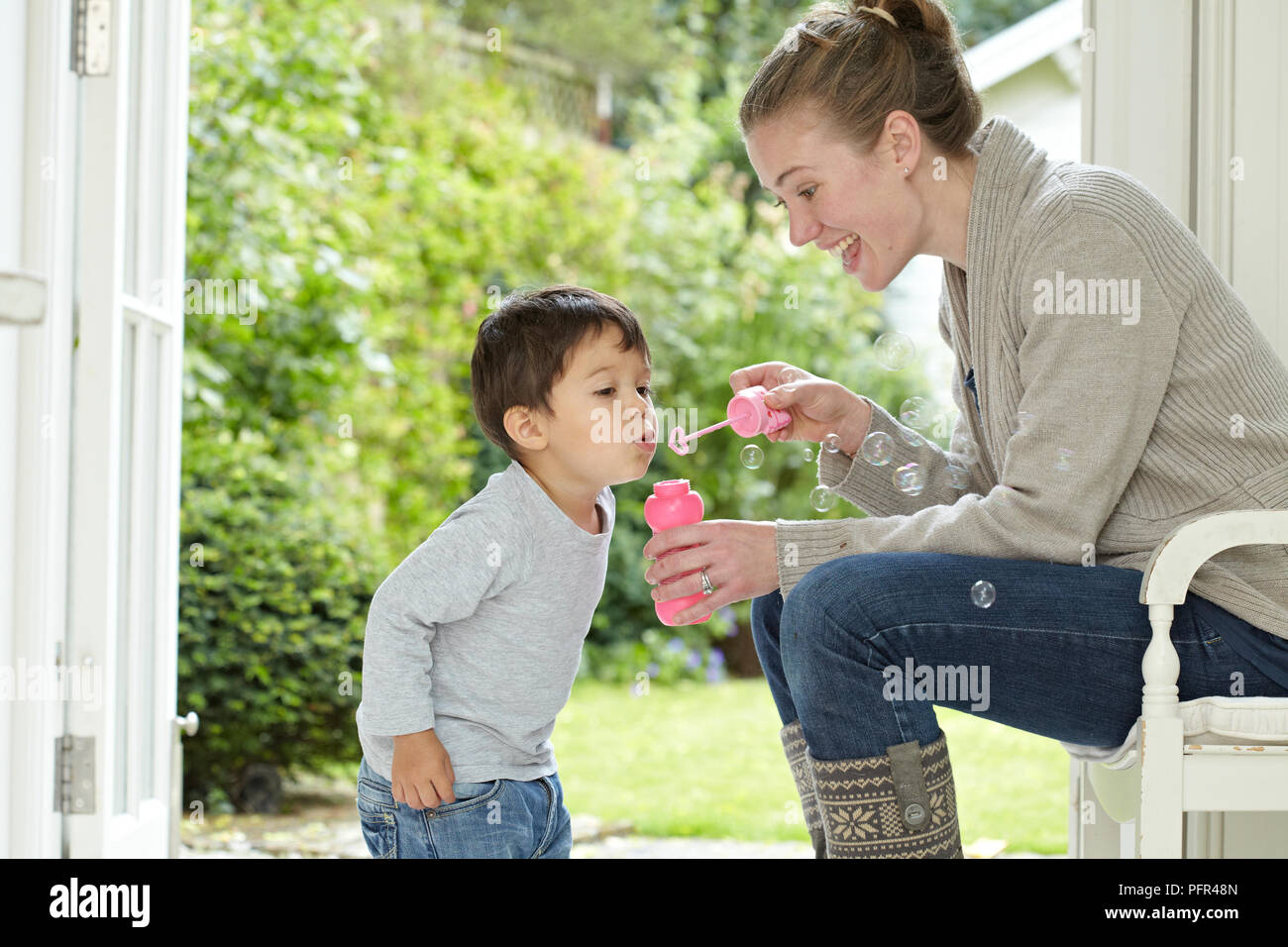 Pequeño niño soplando burbujas, mujer sosteniendo bubble wand Foto de stock