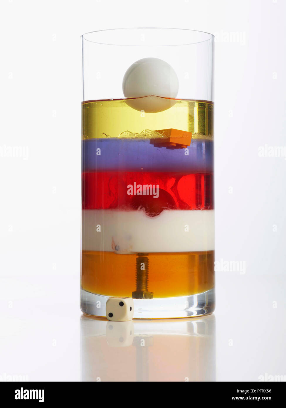 Torre de densidad mostrando jarrón con 5 capas: miel, leche, detergente líquido, agua, aceite vegetal. Perno, tomate cherry, y pelota de tenis de mesa también están en el florero. Foto de stock