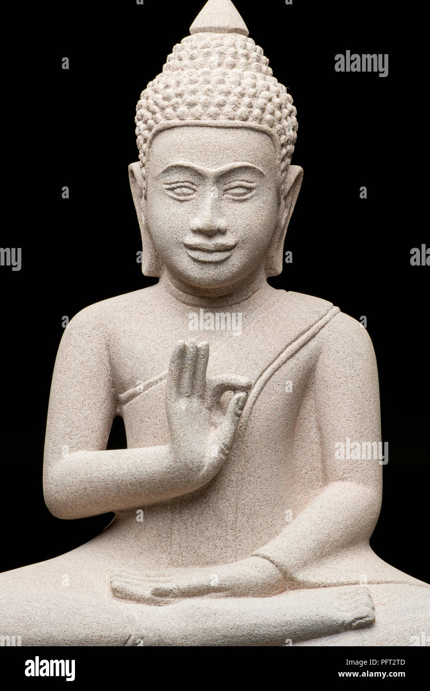 Primer plano de una estatua de Buda sentado de piedra gris con fondo negro haciendo una señal con su mano derecha. Foto de stock