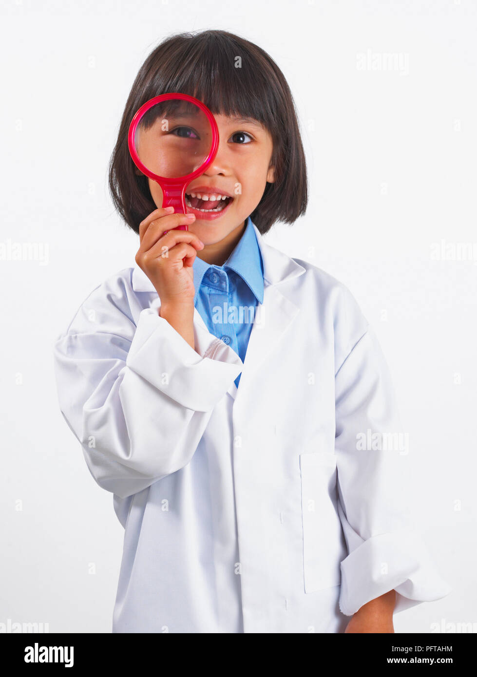 Chica (5 años) en Bata de laboratorio mirando a través de una lupa, vista frontal Foto de stock