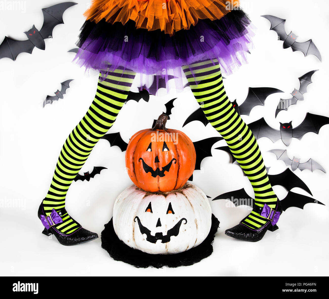 Gracioso negro con rayas verdes en las piernas de una niña con disfraz de Halloween de una bruja con zapatos de bruja y sonriente calabaza de Halloween jack o lantern Foto de stock