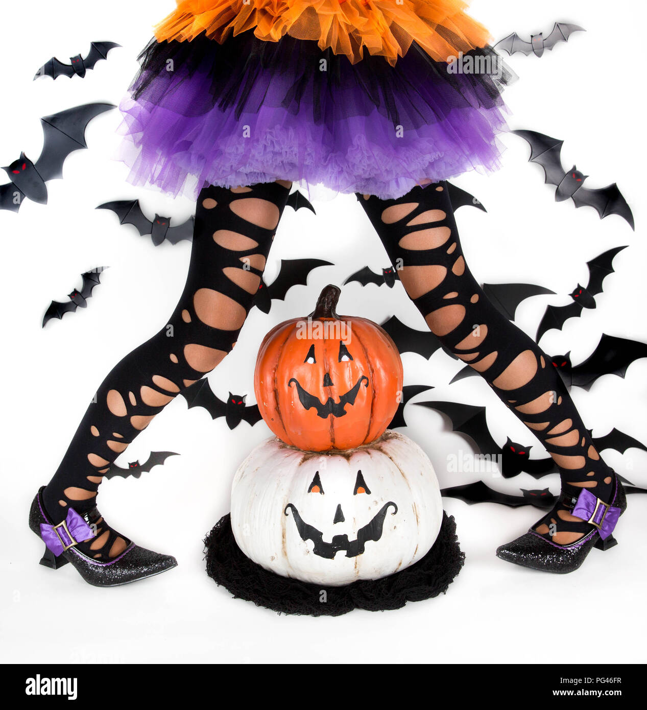 Gracioso ragged las piernas de una niña con disfraz de Halloween de una bruja con zapatos de bruja y sonriente calabaza de Halloween jack o lantern Foto de stock