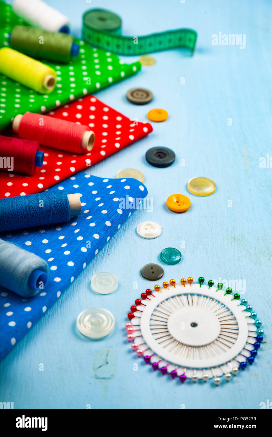 Accesorios de costura y telas multicolores sobre un fondo de madera azul. Telas, cinta métrica, alfileres, botones e hilo. Foto de stock