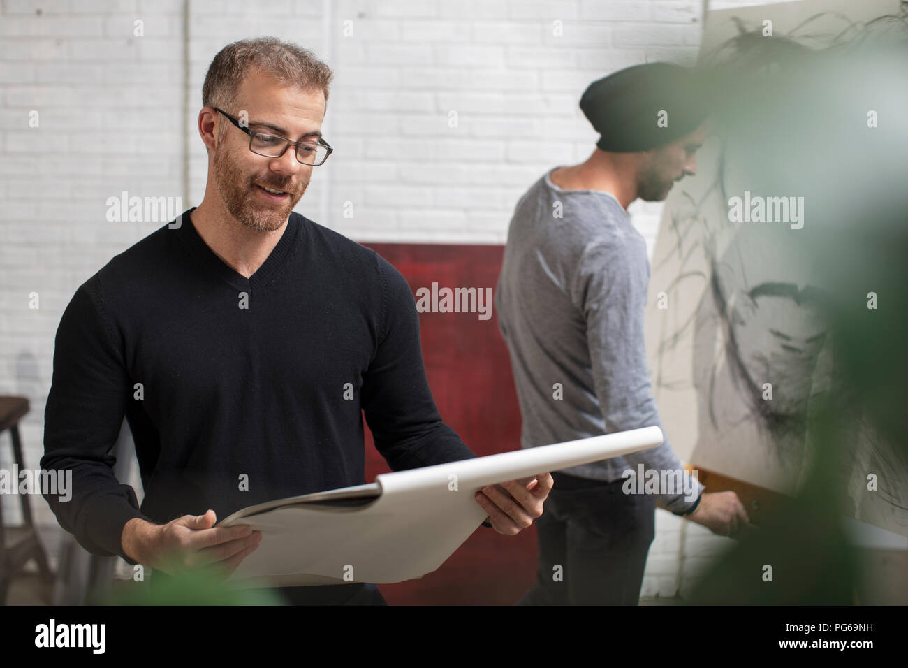 Hombre sonriendo mirando sketchbook en estudio del artista Foto de stock