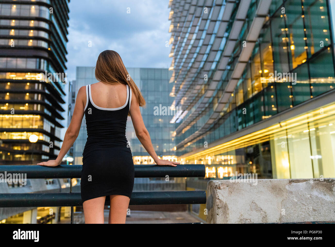 Vista trasera de la joven mujer vistiendo vestido negro en la ciudad al atardecer Foto de stock