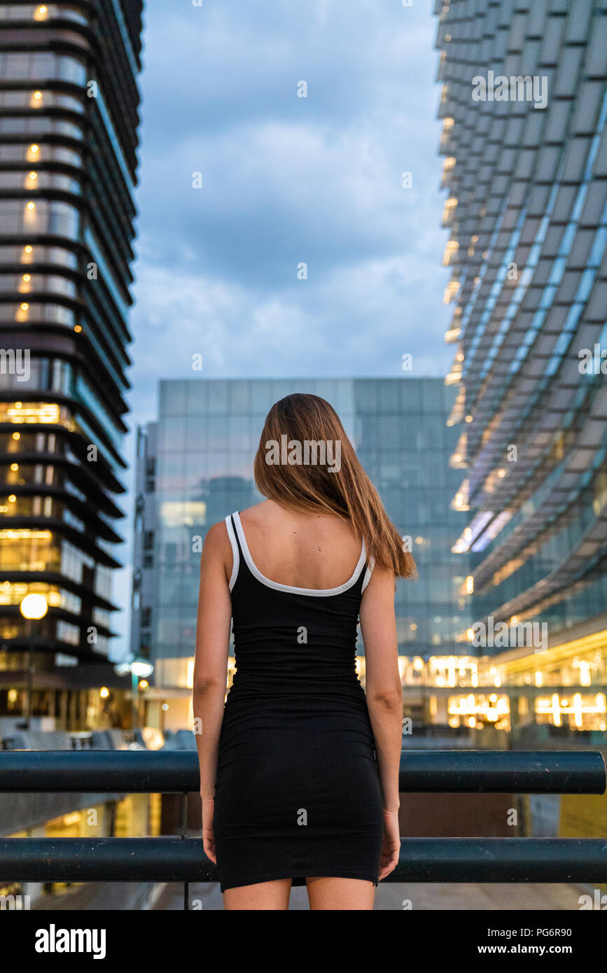 Vista trasera de la joven mujer vistiendo vestido negro en la ciudad al atardecer Foto de stock