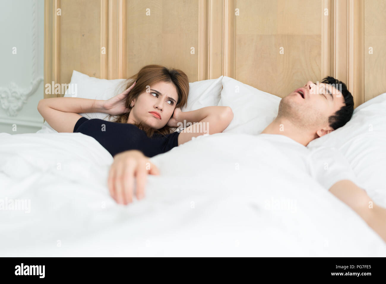 Molesto Asian wife bloqueando sus oídos del ruido del marido de ronquidos en la habitación en la casa. Pareja joven tiene un problema con los ronquidos del hombre. Foto de stock