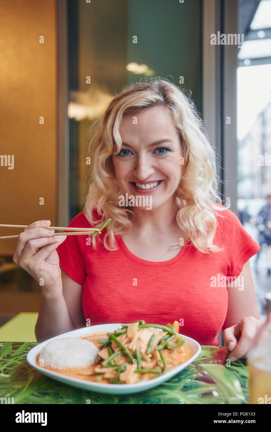 Retrato de mujer rubia sonriente comer vegetariano plato Asiático Foto de stock