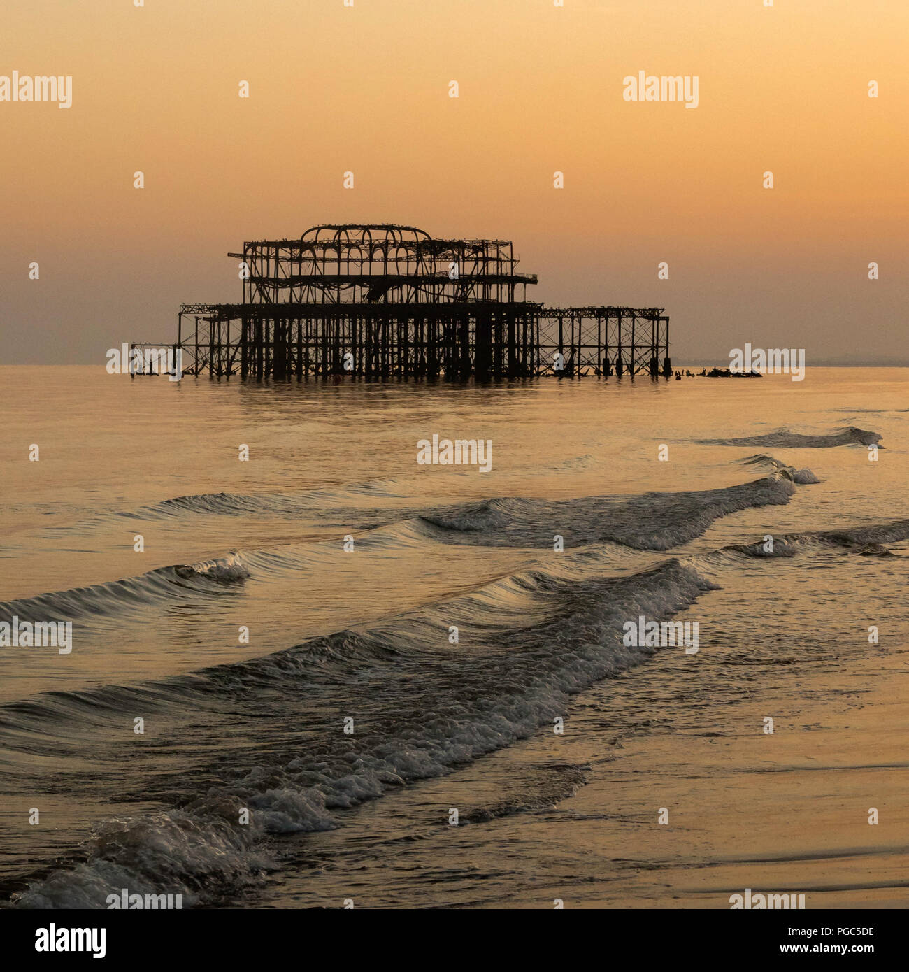 La larga exposición a la puesta de sol sobre Brighton's Old West Pier con olas rompiendo en la orilla, Brighton, East Sussex, Inglaterra Foto de stock