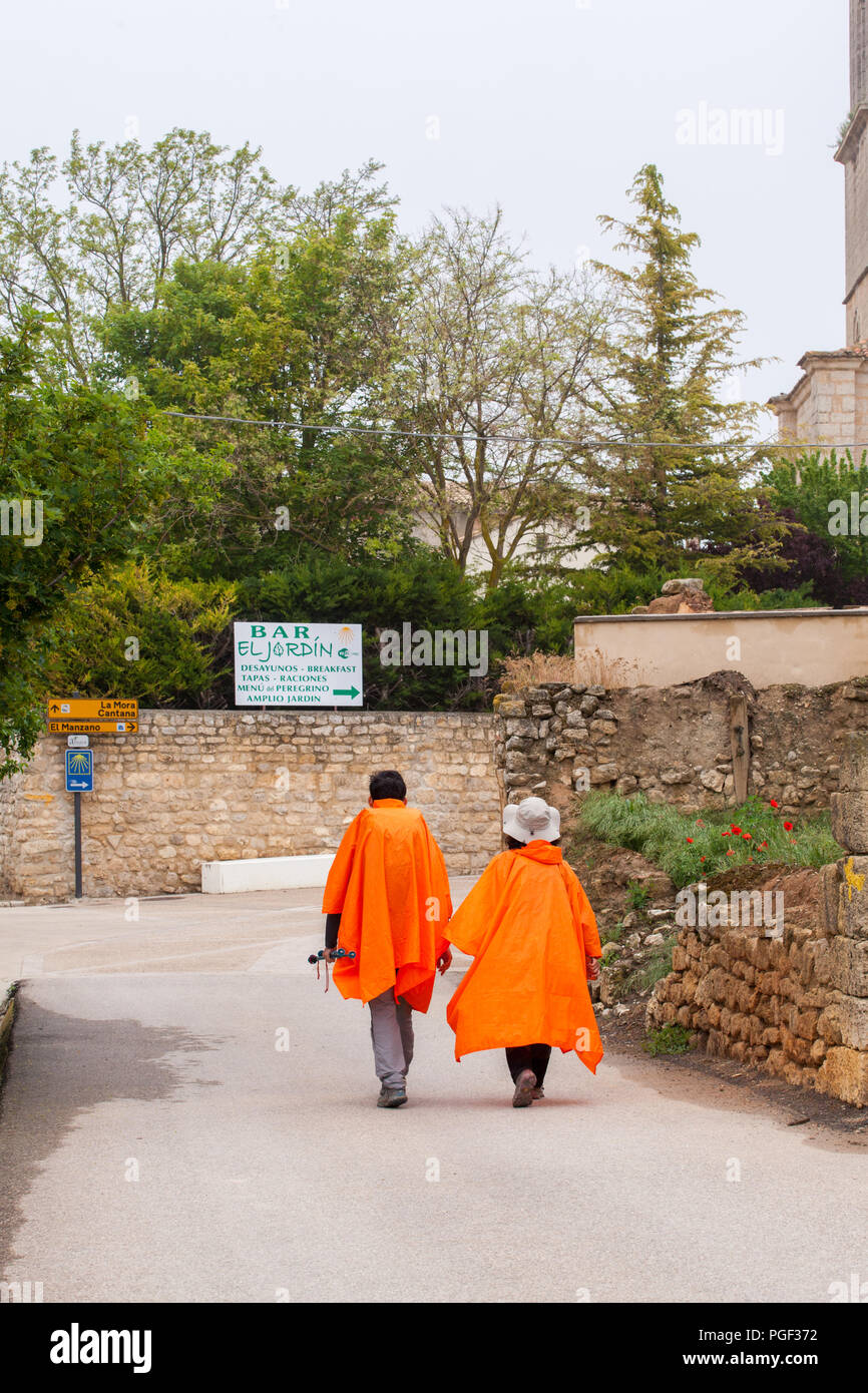 Dos peregrinos que llevan poncho de color naranja y húmedo a pie en la  ciudad de Castrojeriz mientras caminan por el Camino de Santiago por el  Camino de Santiago Fotografía de stock -