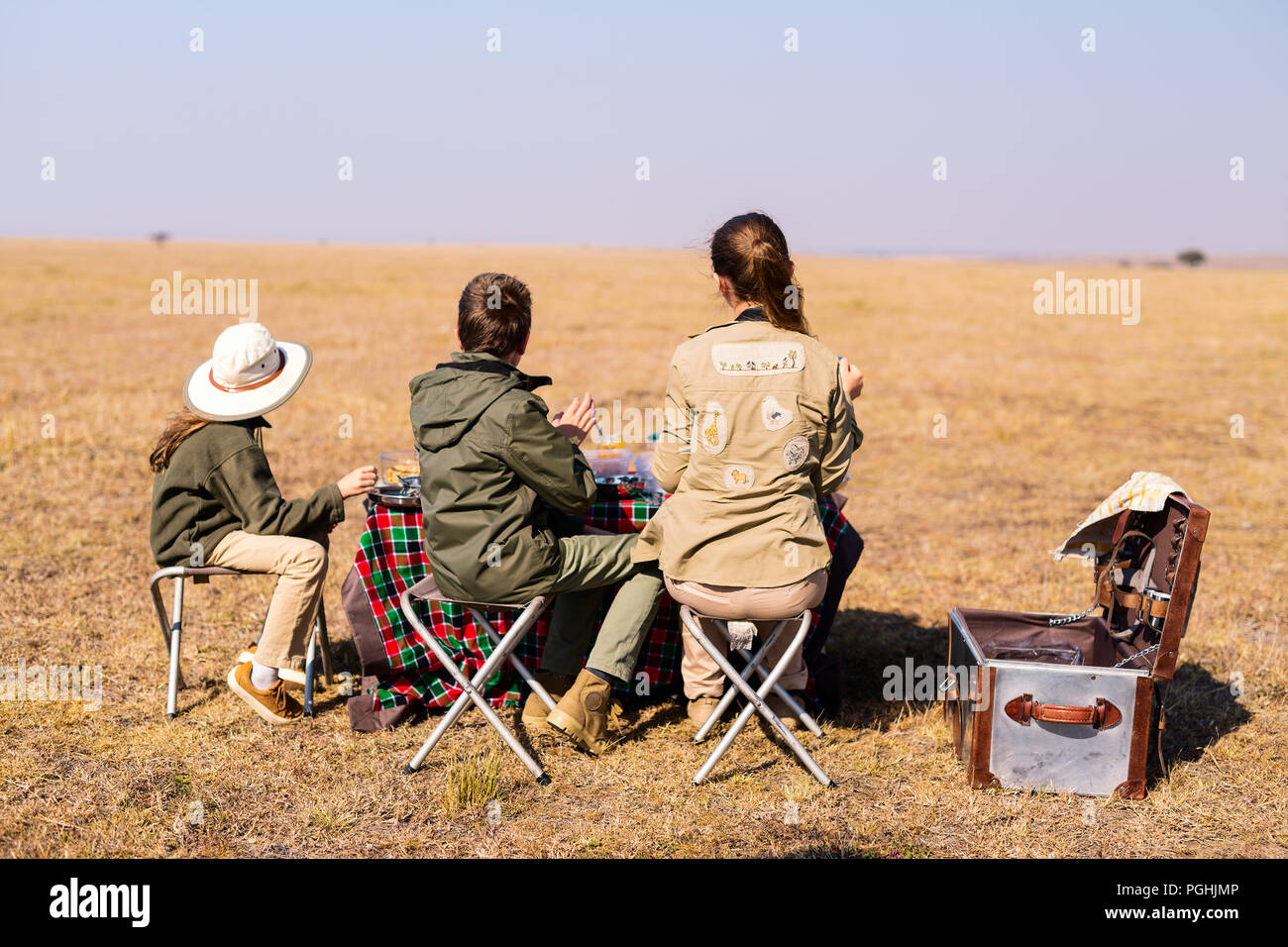 Vista posterior de la madre de familia y niños en safari africano vacaciones disfrutando de desayuno bush Foto de stock
