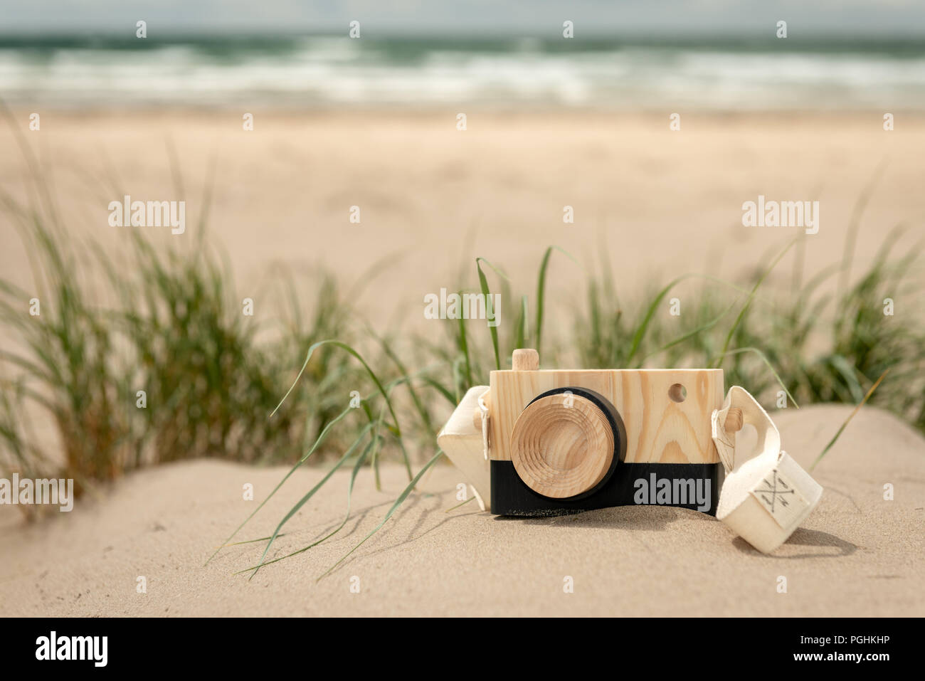 Cámara de fotos de juguete de madera en la vista de nivel bajo de la duna de arena en día soleado brillante con fondo de playa vacío desenfocado como concepto de verano. Foto de stock