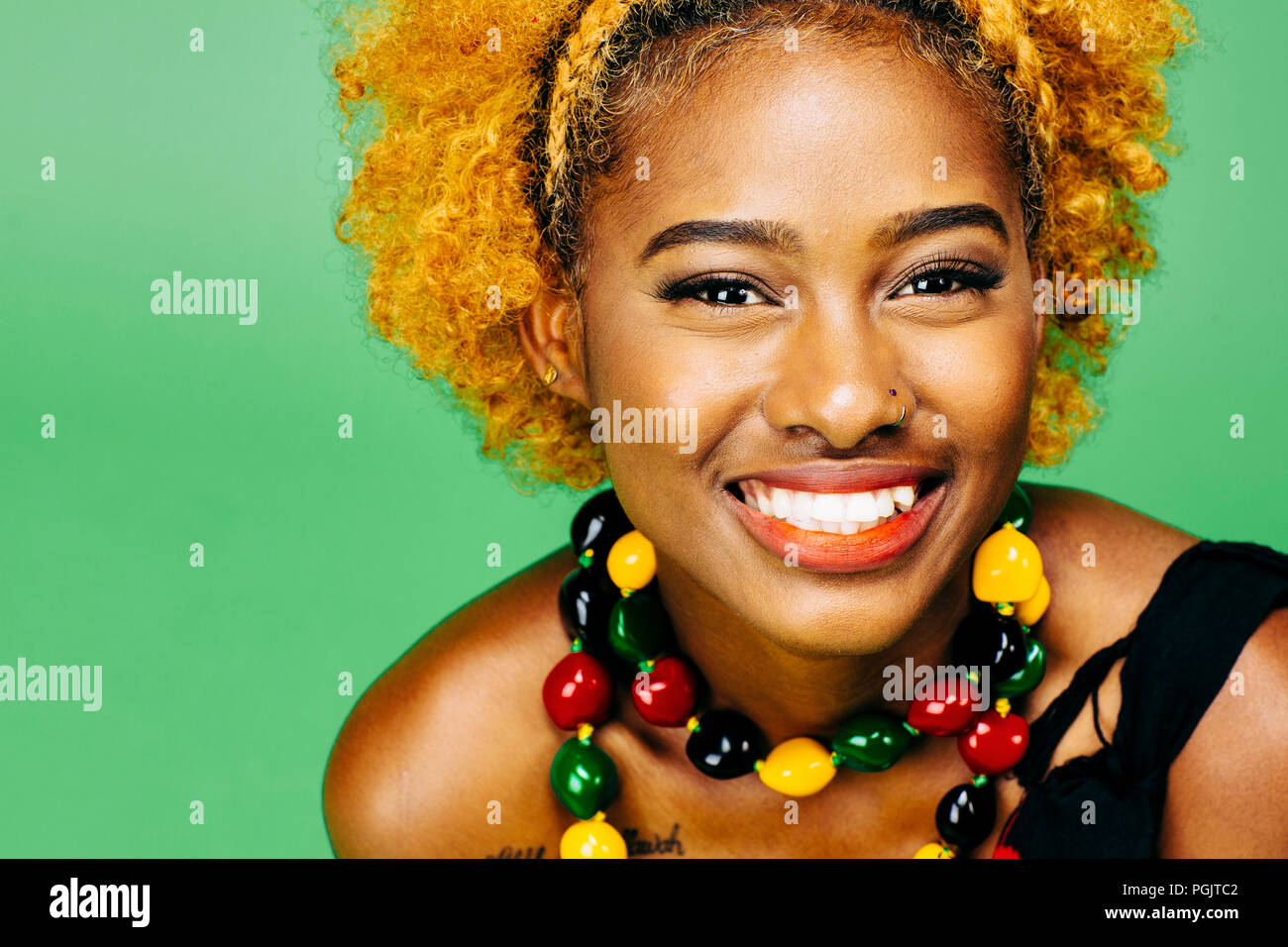 Cerca de un feliz joven con grandes sonrisas y collar de colores, delante de un fondo verde Foto de stock