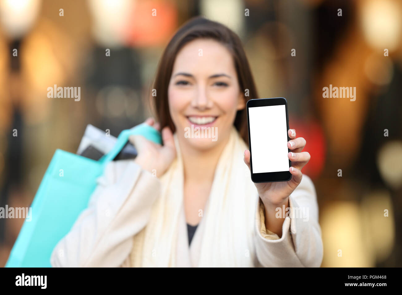 Happy shopper mostrando una pantalla vacía del teléfono maqueta afuera en la calle con un escaparate en el fondo Foto de stock