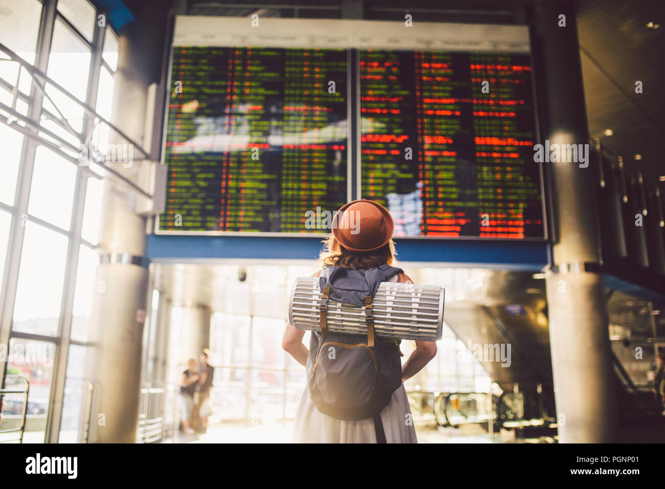 Tema viajar en transporte público. mujer joven de pie con la espalda en el vestido y el sombrero detrás de mochila y equipo de camping para dormir, esterilla aislante buscar Foto de stock