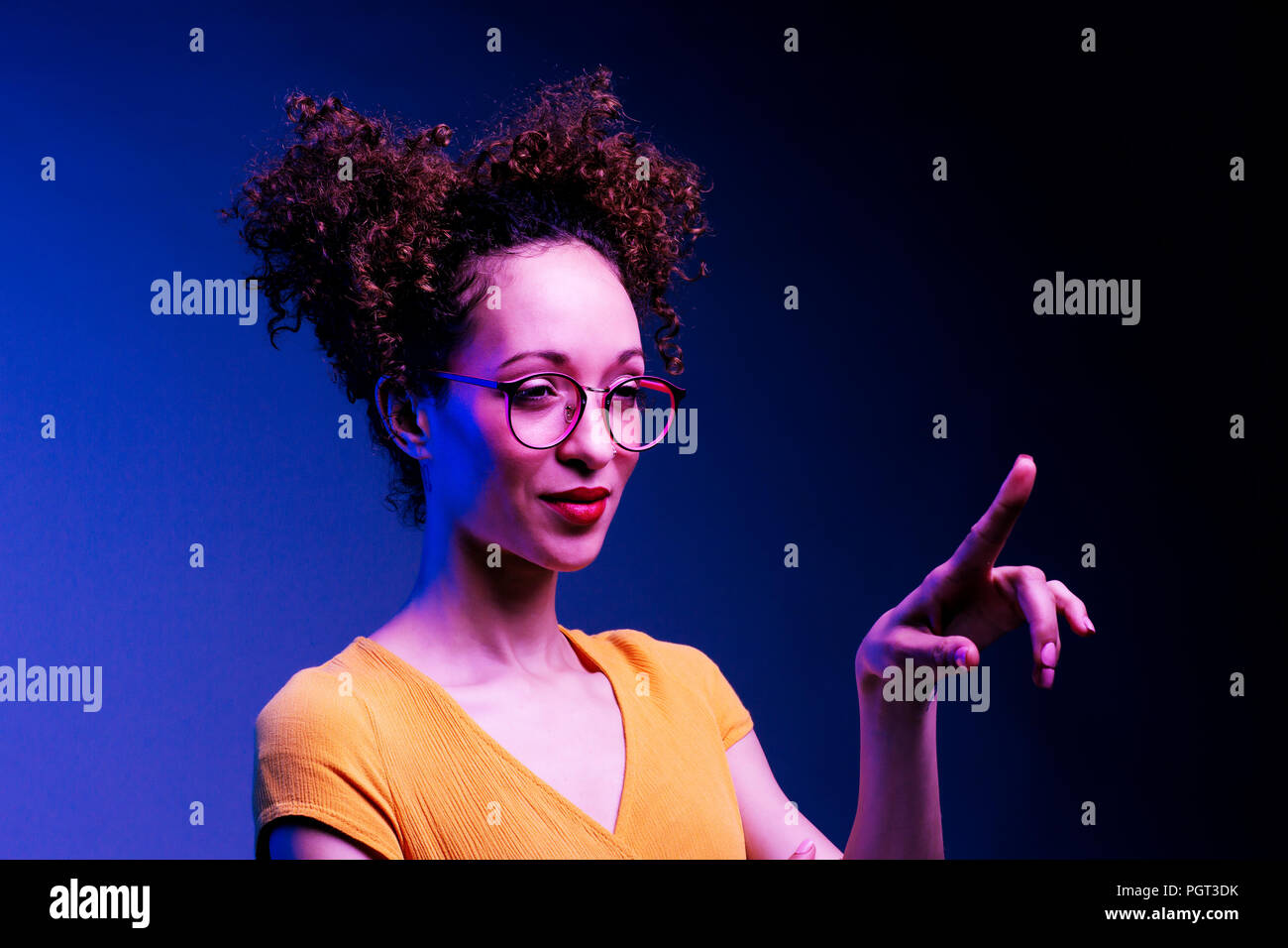 Chica inteligente con gafas y con el dedo levantado sobre pulsar o punto en algo, aislado sobre fondo azul oscuro Foto de stock