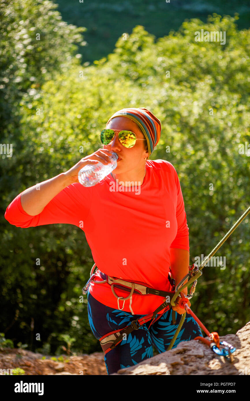 Foto de mujer escalador en gafas de sol agua potable sentado Foto de mujer sonriente escalador con gafas de sol sentado