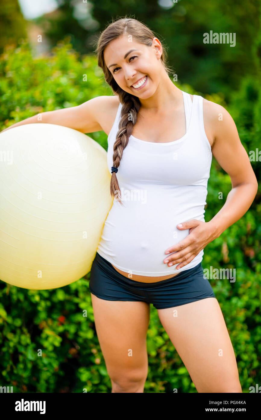 Mujer embarazada feliz tocando el abdomen mientras sostiene la bola de Fitness Foto de stock