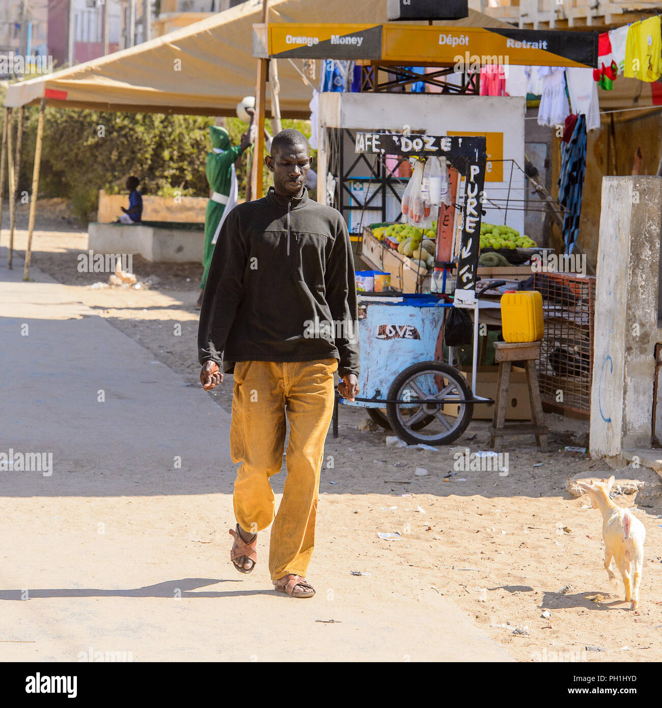 SAINT LOUIS, SENEGAL - Apr 24, 2017: No Identificado hombre senegalés en camisa negra y pantalones mostaza camina al lado de la cerca de la tienda en Saint Louis Fotografía de stock - Alamy