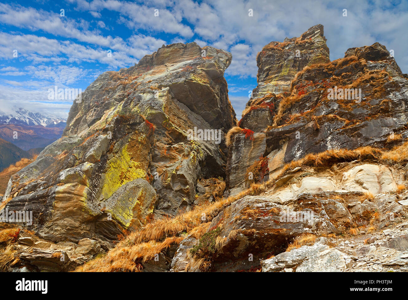 Enormes rocas cubiertas con vegetación amarillo y rojo con el cielo azul y las nubes blancas en el fondo, en la ladera del monte Chandrashila, Himalaya Foto de stock