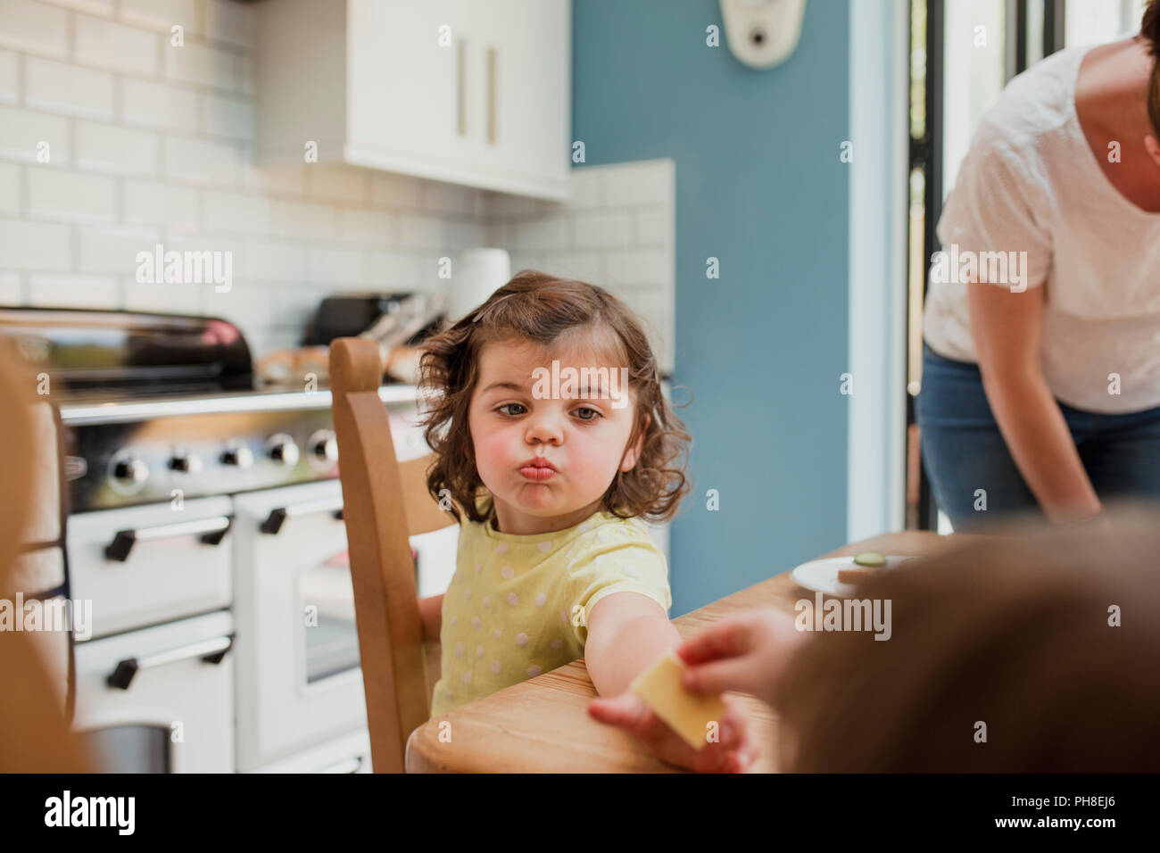 Punto de vista angular de una niña que se entregan algunos alimentos en la mesa de la cocina. La niña se centra en la comida y las migajas a su alrededor mou Foto de stock