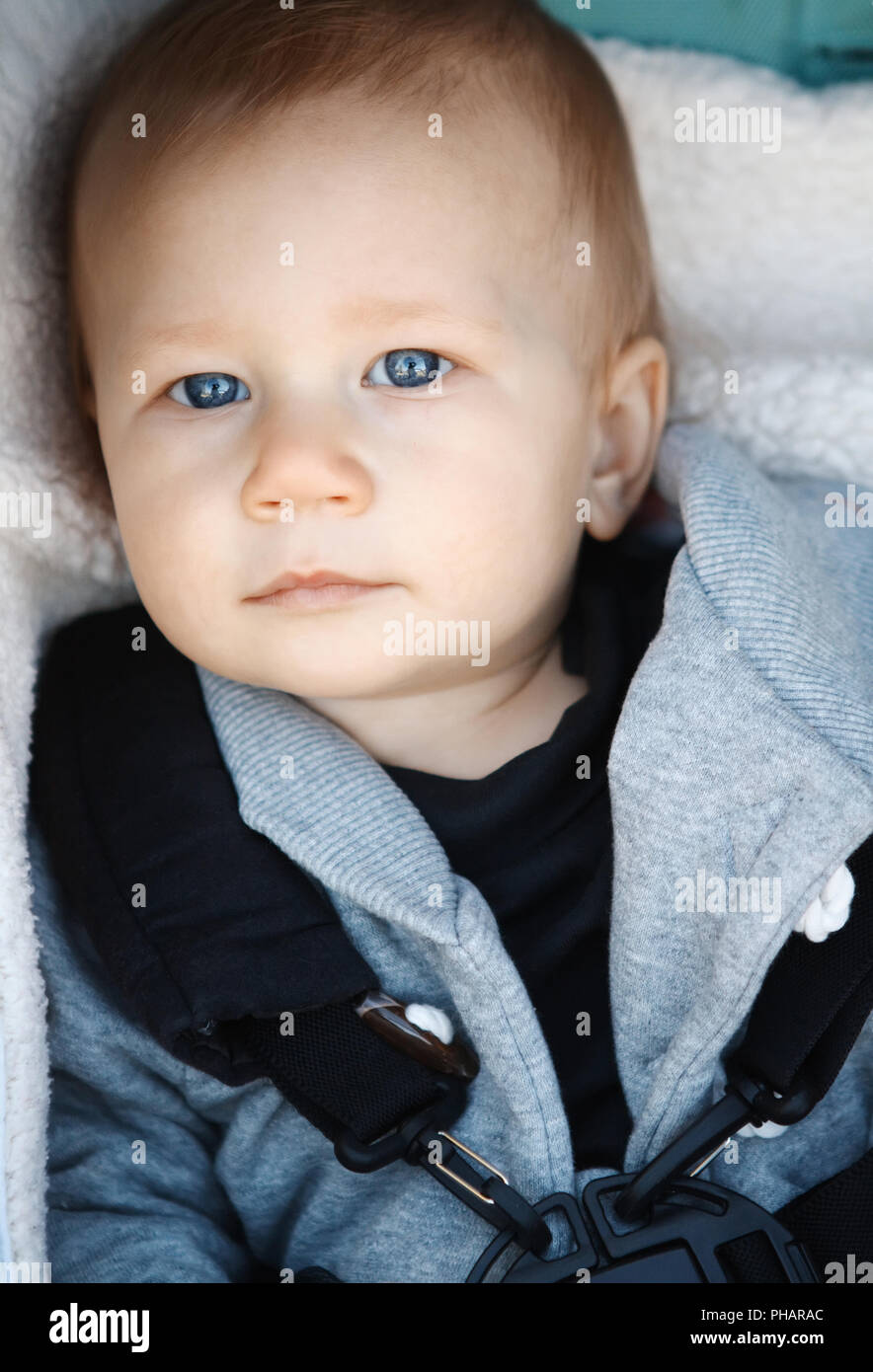 Retrato de lindo gracioso adorable caucásica con ojos azules de bebé sentado en la silla de paseo mirando en cámara, de seguridad abrochados por razones seguridad de stock -