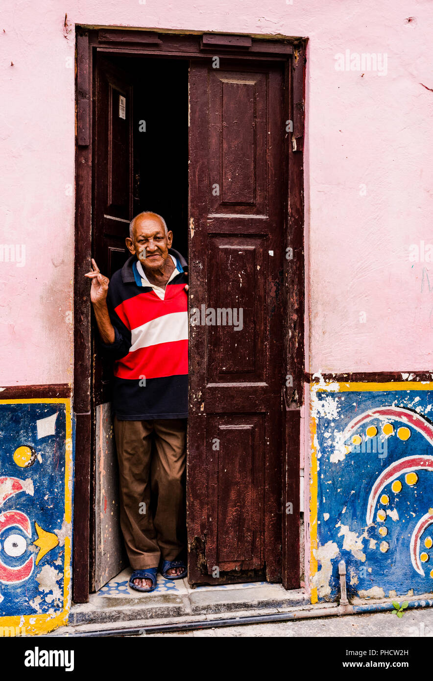 Edad hombre cubano mira a través de la puerta abierta de la casa colonial en la Habana Vieja, Cuba. Foto de stock