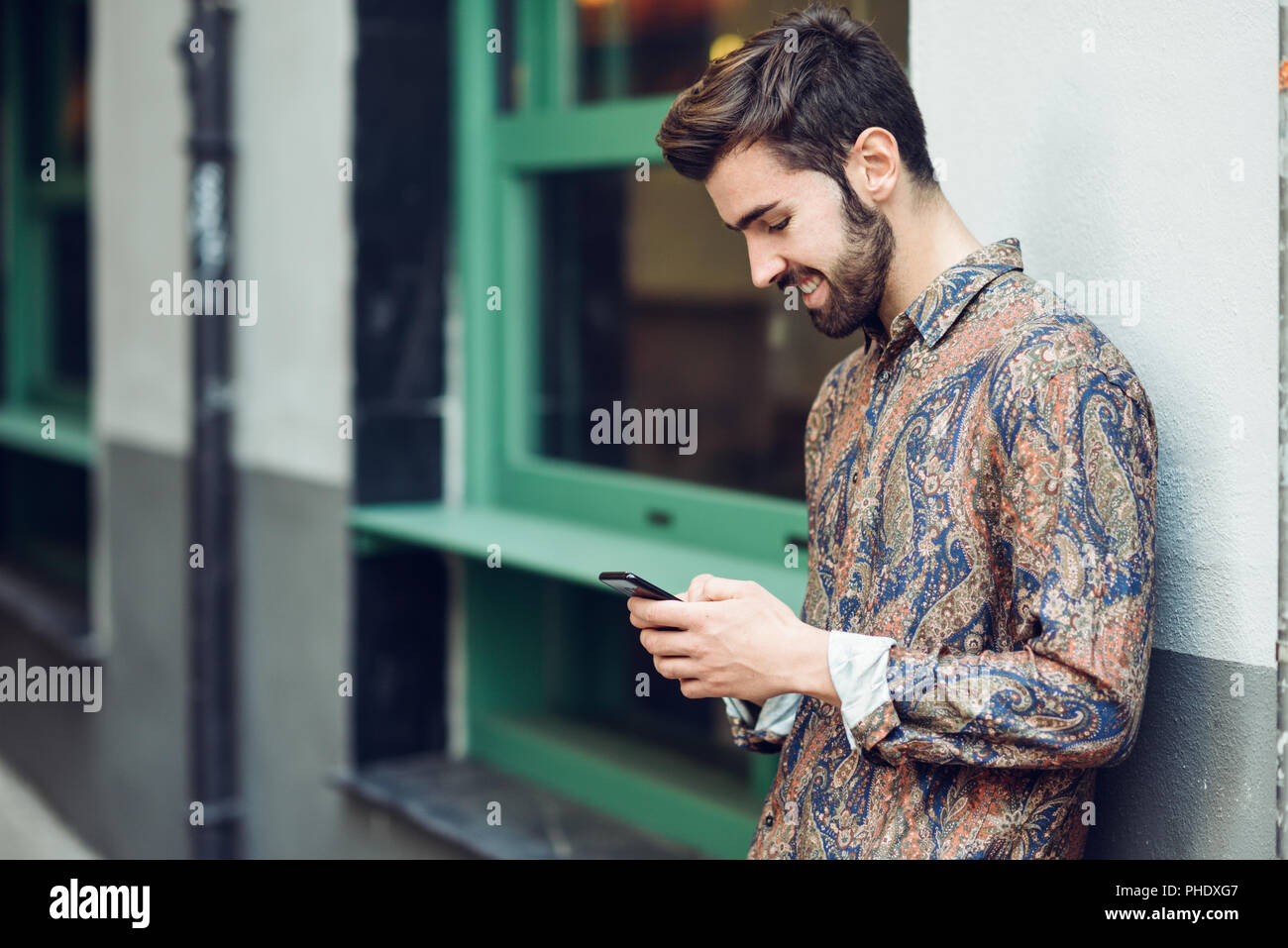 Hombre sonriente joven vistiendo ropa casual mirando su en la calle. con y peinado moderno en el contexto urbano Fotografía de stock - Alamy