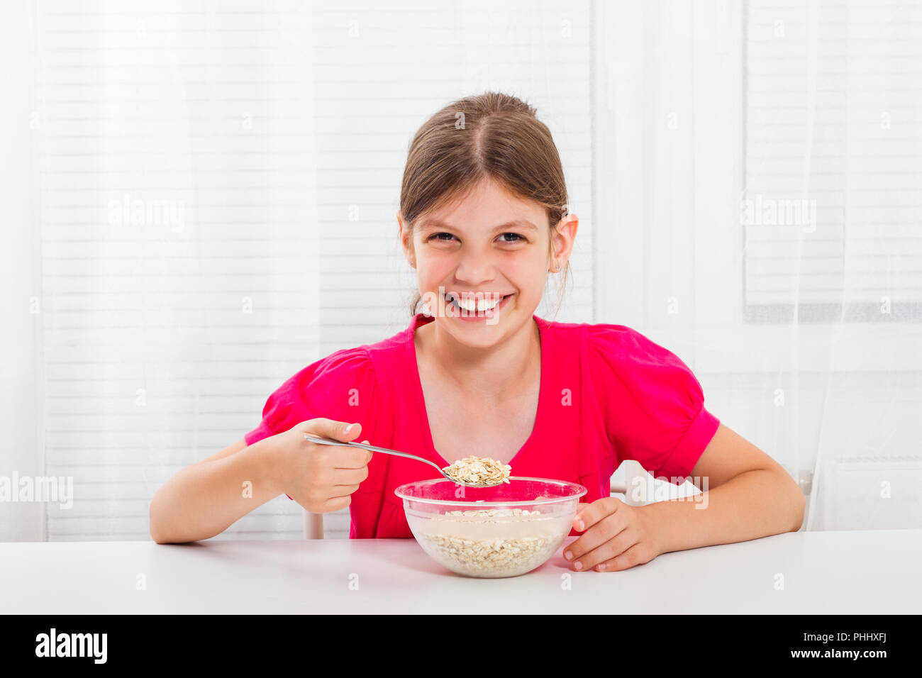 Cute Little Girl está sentado a la mesa y comiendo cereales para el