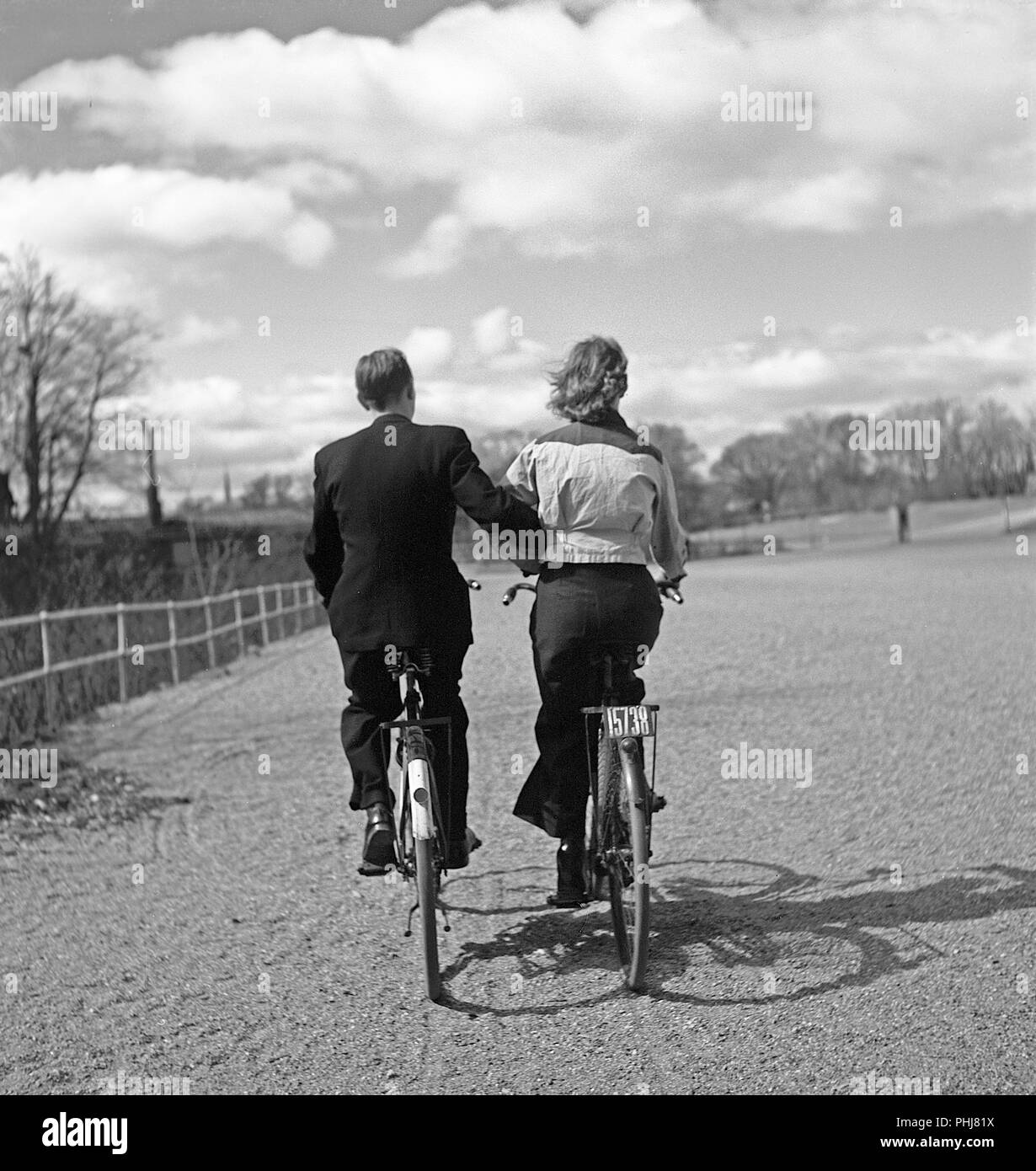 1940 par de bicicletas. Una joven pareja está montando sus bicicletas en un soleado día de primavera. En el amor como lo son, están llevando armas, incluso cuando en sus bicicletas. Observe que el signo de registro en su bicicleta, ya que este tema era obligatorio para demostrar que usted paga impuestos de bicicletas. Suecia 1942. Foto Kristoffersson un88-5 Foto de stock