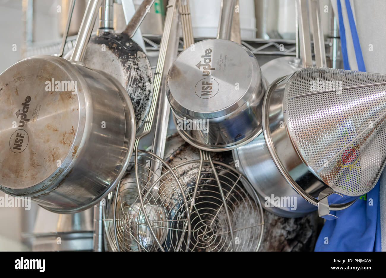 Un grupo de acero inoxidable ollas, sartenes y coladores colgando en una cocina comercial Foto de stock