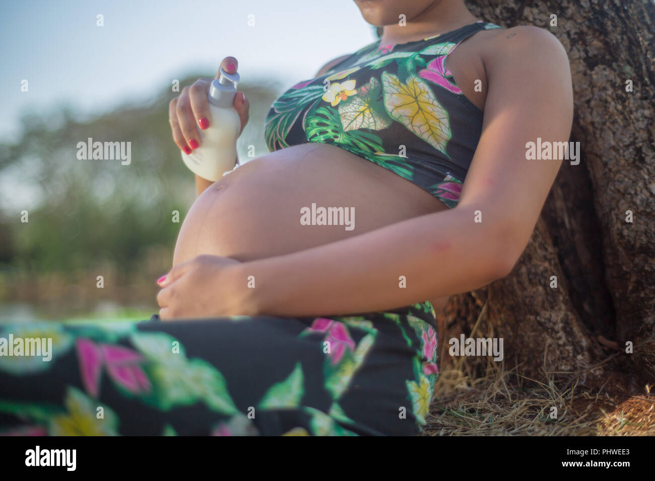 La mujer embarazada en un parque poner crema en su vientre para evitar las estrías. Foto de stock