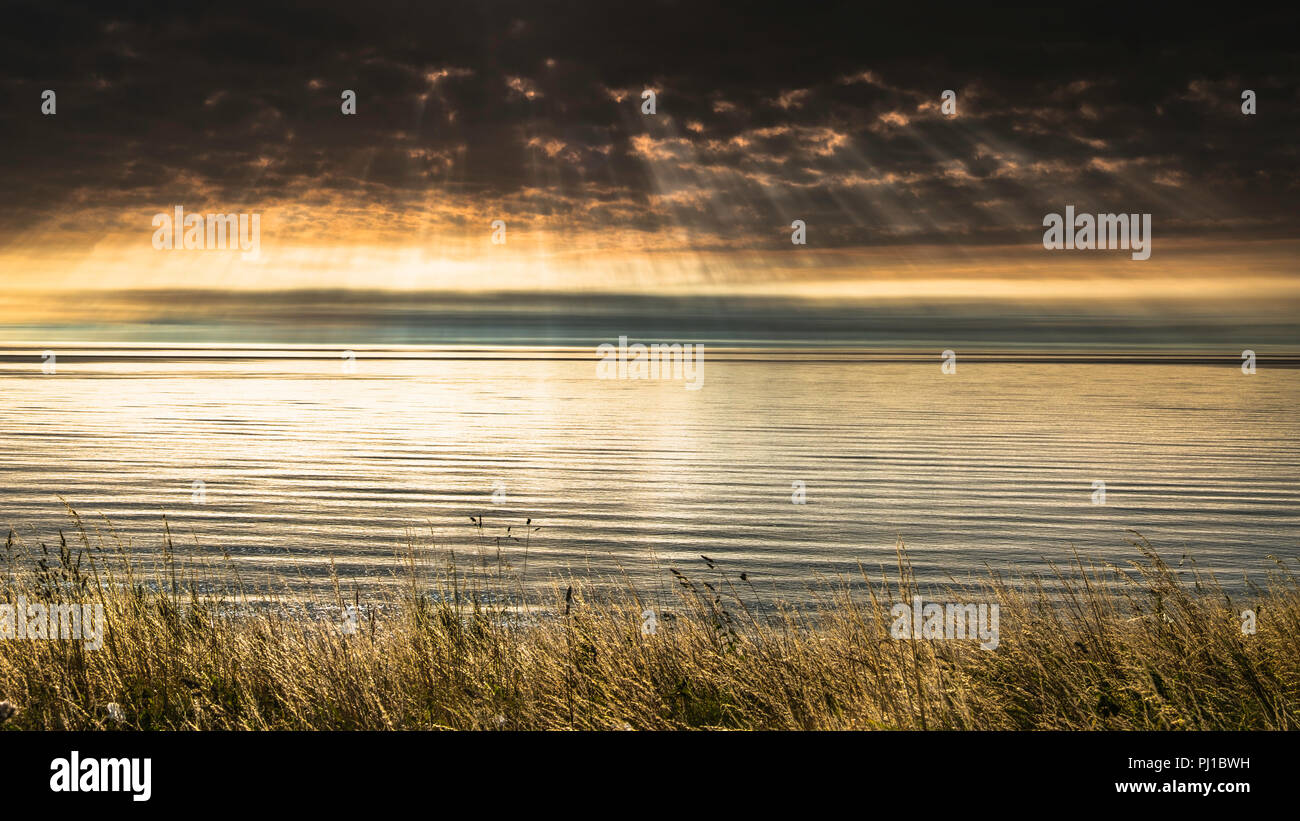 Rayos crepusculares forma sobre un tranquilo mar del Norte. Foto de stock