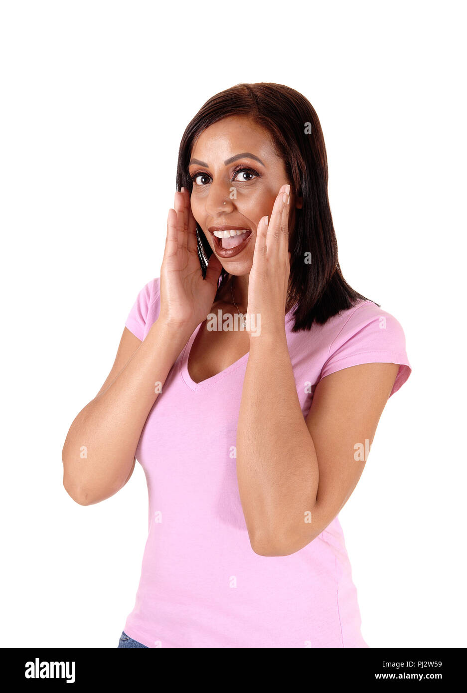 Un joven sorprendido de pie con sus manos sobre su cara y una boca abierta, en camisa rosa, aislados en fondo blanco. Foto de stock