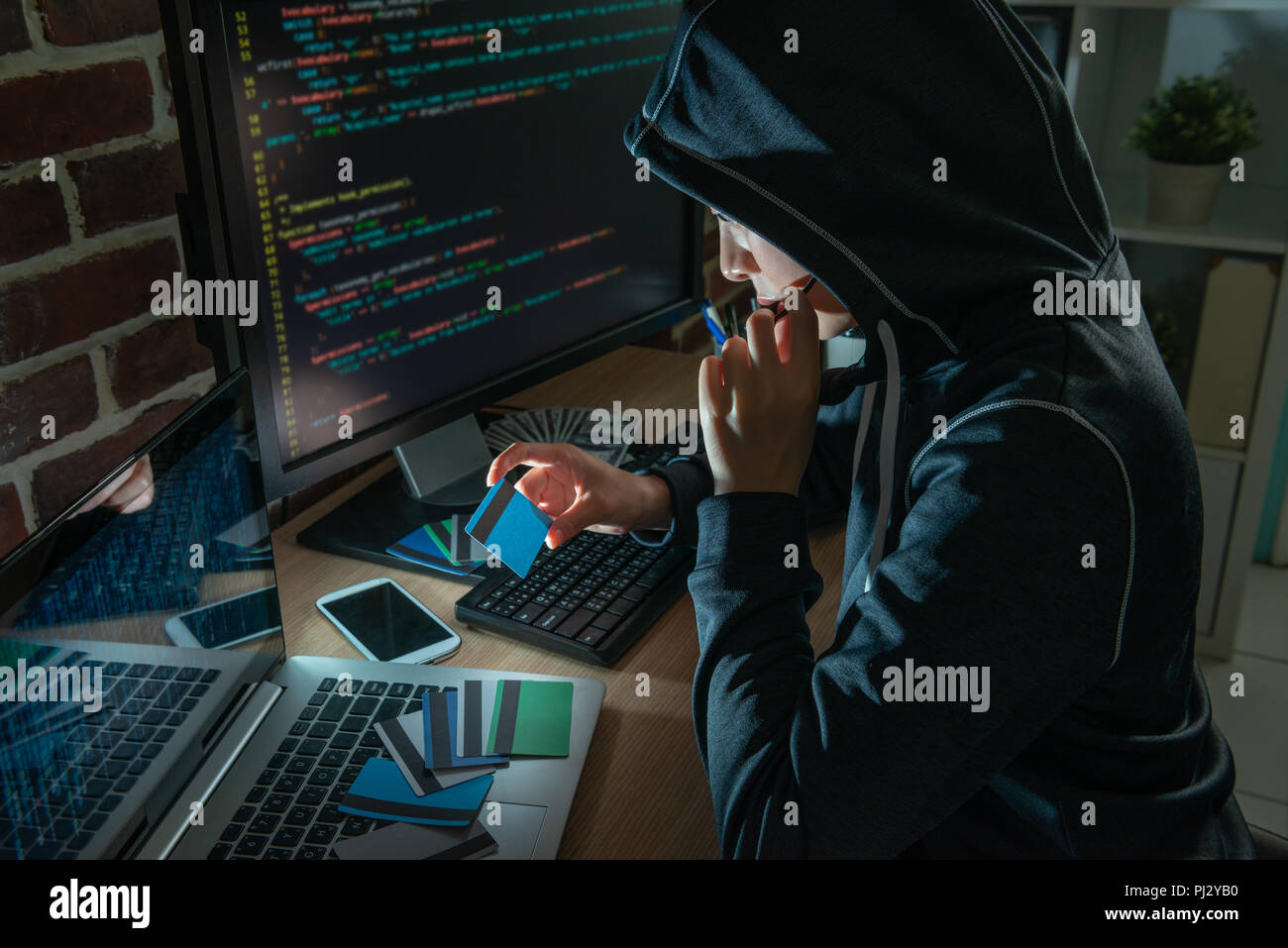 El hoodie hacker mirando tarjetas bancarias robadas. Planificación para irrumpir en las víctimas y teniendo en cuenta el dinero. Foto de stock