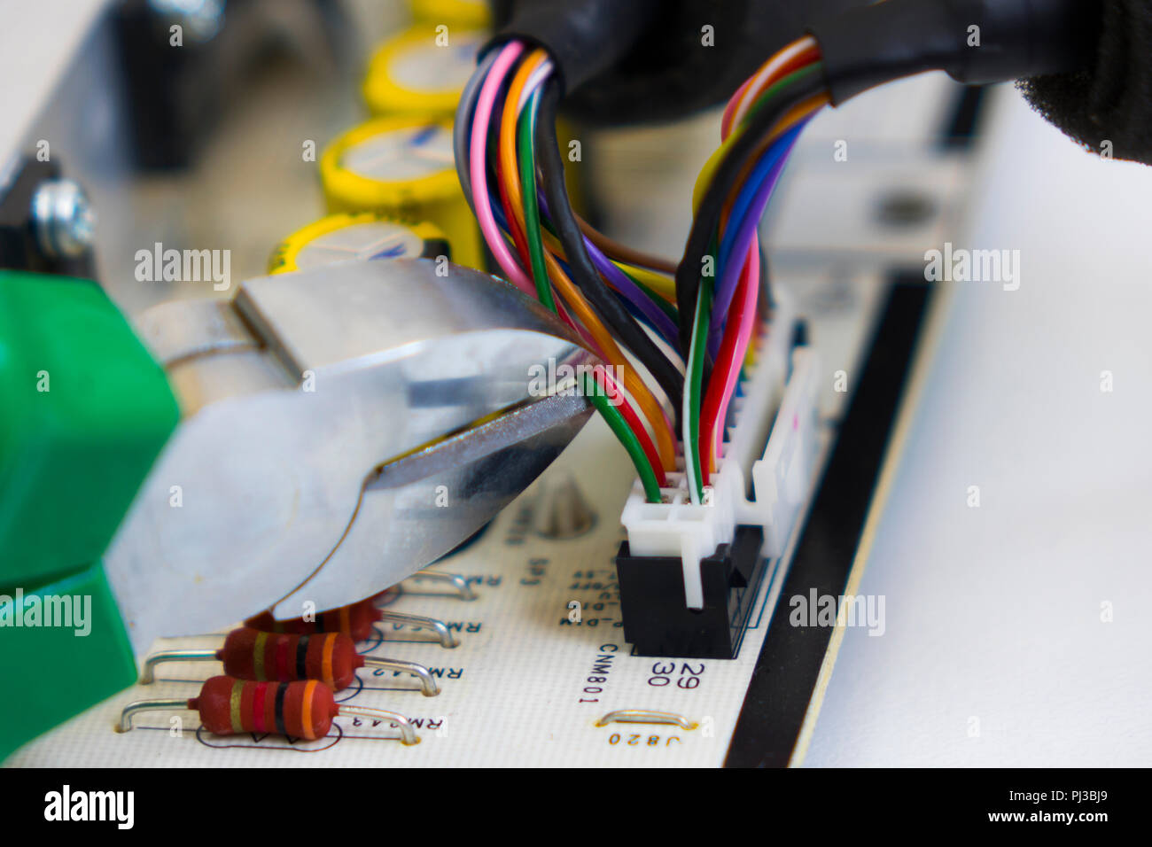 Desmontaje bomba electrónica, pinzas para cortar el cable rojo en un manojo de hilos de color sobre el trasfondo de la motherboard o chip electrónico Foto de stock