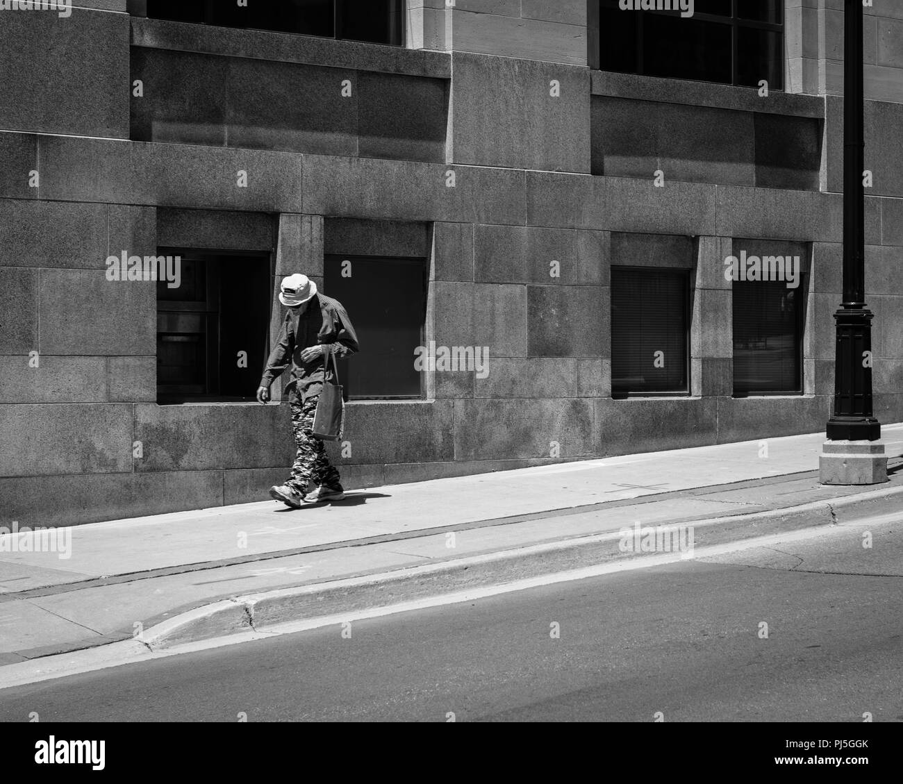 El viejo caminaba por la calle cerca de un edificio en blanco y negro Foto de stock