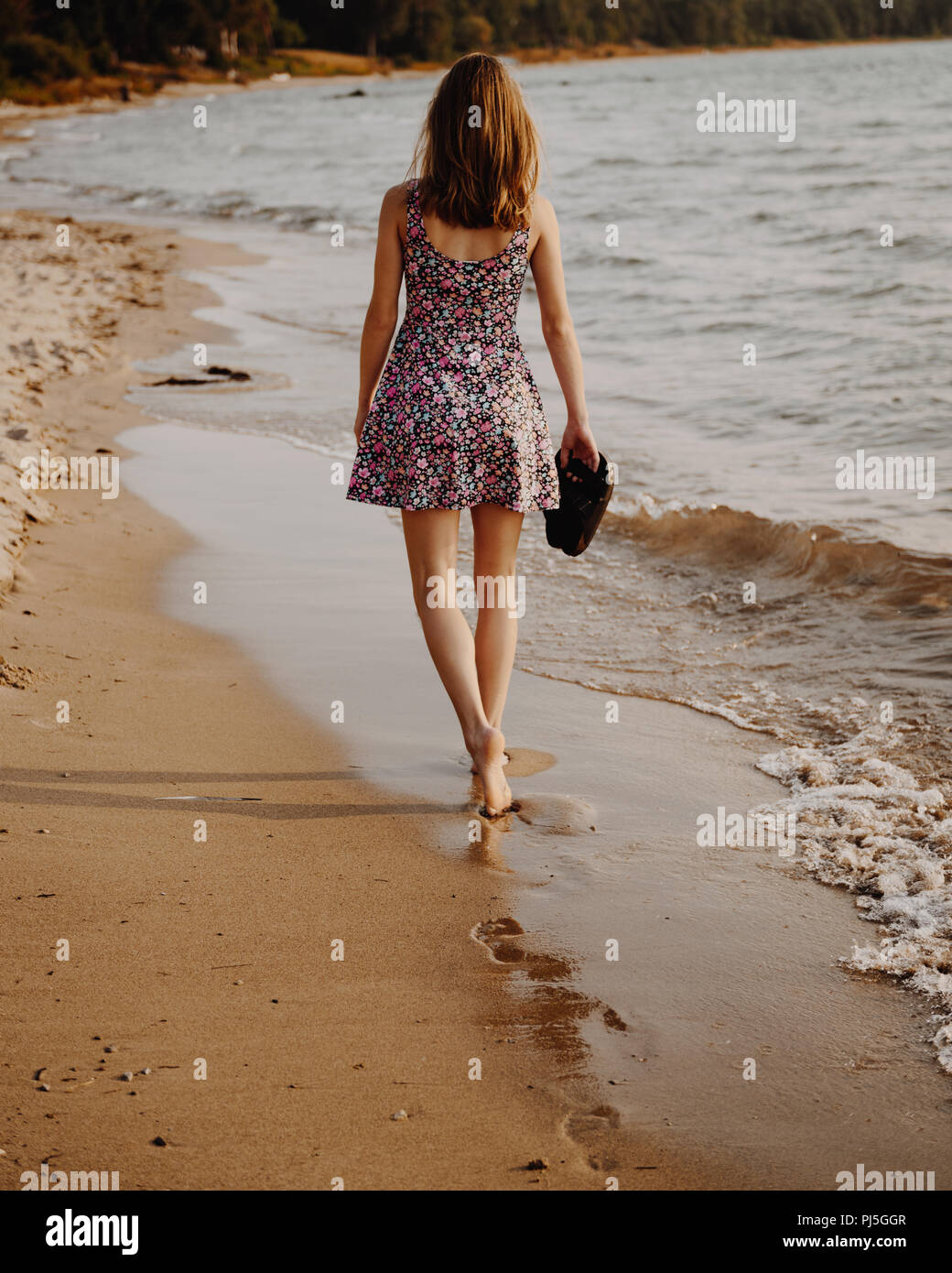 Adolescente Paseando por la playa al atardecer, sosteniendo sus sandalias Foto de stock