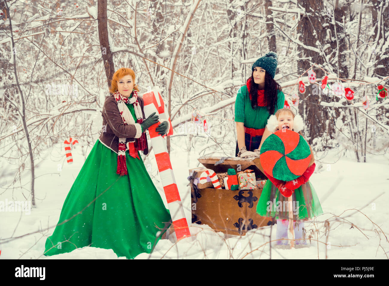 En la familia tradicional de Navidad disfraces de flores, Rojo - Verde ,  elfos ayudantes de Santa Claus, en el bosque de invierno con un cofre de  regalos y un enorme candy