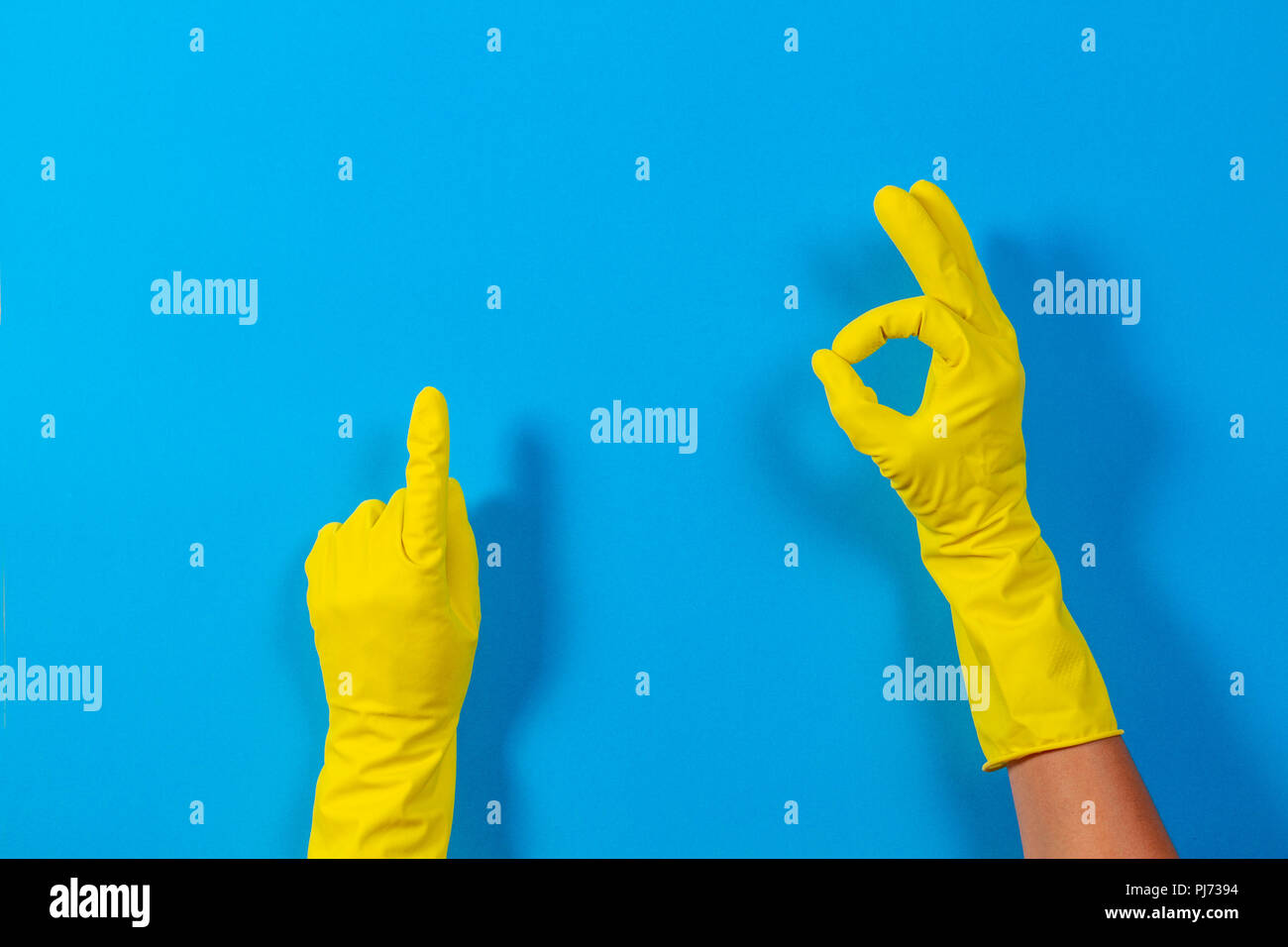 Mujer de manos con guantes de goma amarilla haciendo un gesto significado  ok y señala hacia arriba con el dedo, fondo azul Fotografía de stock - Alamy