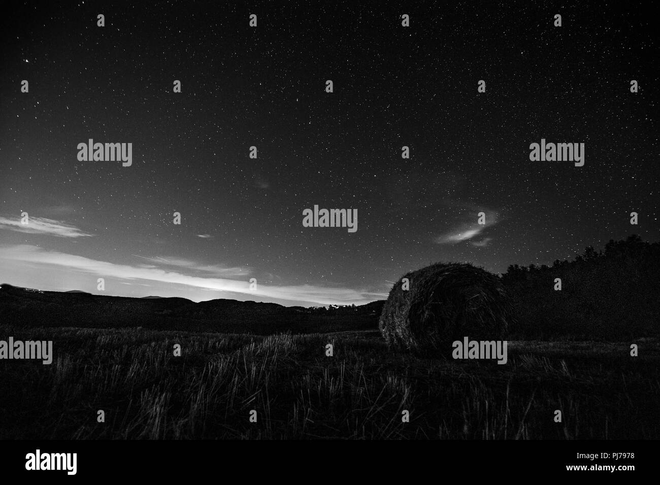 Hermosa vista del cielo nocturno estrella con nubes sobre un campo cultivado con fardos de heno Foto de stock