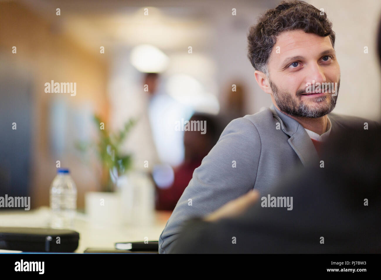 Empresario sonriente escuchando a un colega en la oficina Foto de stock