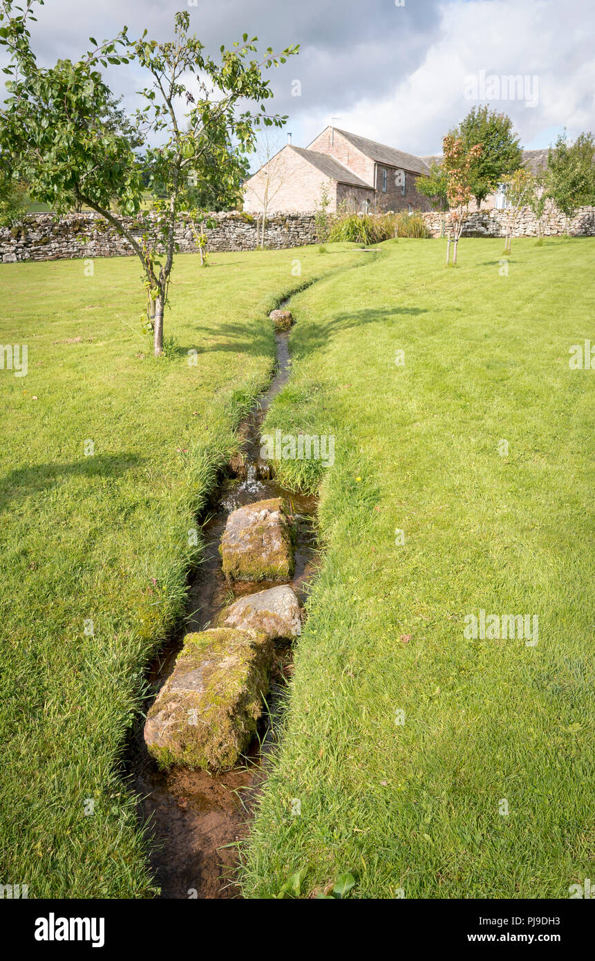 Un arroyo de agua fluye hacia abajo a través del gran jardín en Blencowe Hall dando la apariencia de un arroyuelo, en Cumbria, Reino Unido Foto de stock