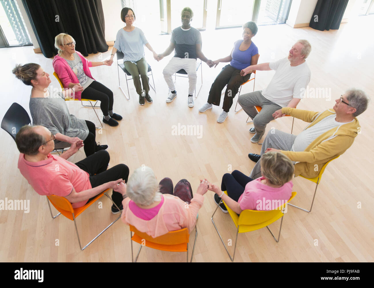 Active los ancianos tomados de la mano en círculo, meditando en el centro comunitario Foto de stock