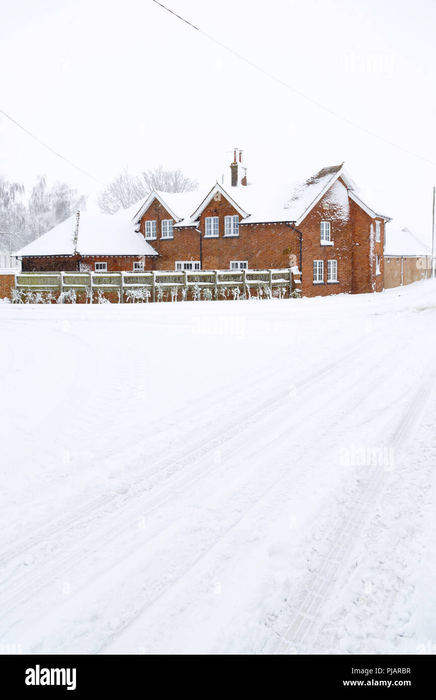 Una estancia de estilo victoriano en invierno con la carretera cubierta de nieve en primer plano. Inglaterra, Reino Unido. Foto de stock