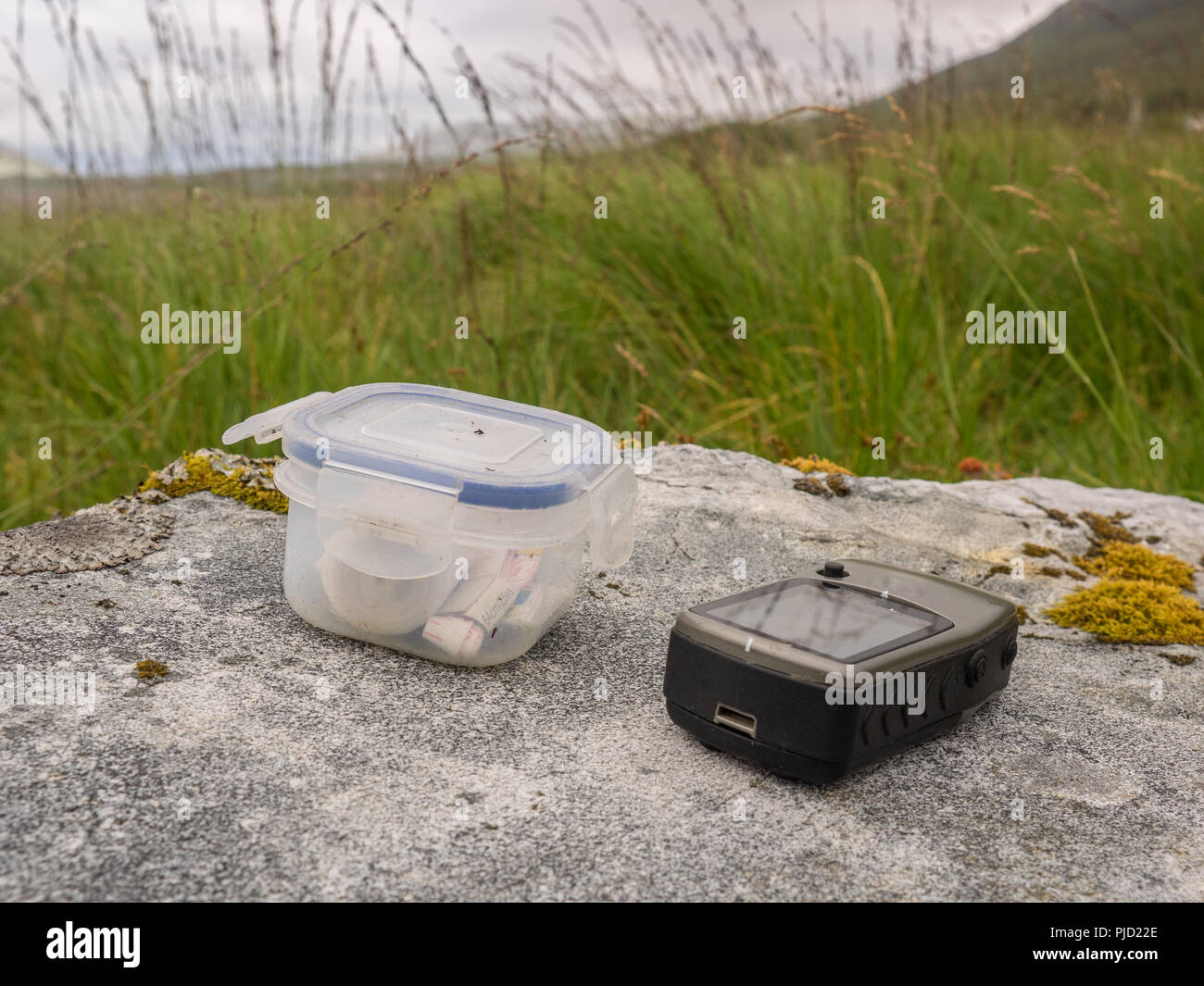 Geocache con dispositivo GPS en una gran roca con fondo de pasto Foto de stock