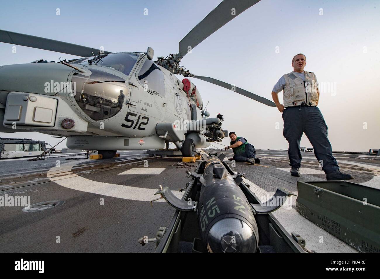 5ª Flota de EE.UU. ZONA DE OPERACIONES (18 de julio de 2018) la aviación Mecánica Estructural de primera clase, Thomas Hall, a la derecha, y la aviación Técnico Electrónico 2ª clase Michael Maye, asignada a las "víboras" huelga marítimo escuadrón de helicópteros (HSM) 48, se preparan para cargar un misil AGM-114 Hellfire en un helicóptero MH-60 Seahawk R en la cubierta de vuelo del misil guiado por el destructor USS Jason Dunham (DDG 109). Jason Dunham está desplegado en los EE.UU. 5ª Flota de la zona de operaciones en apoyo de las operaciones navales para garantizar la estabilidad y la seguridad marítima en la región central, que conecta el Mediterráneo y el P Foto de stock