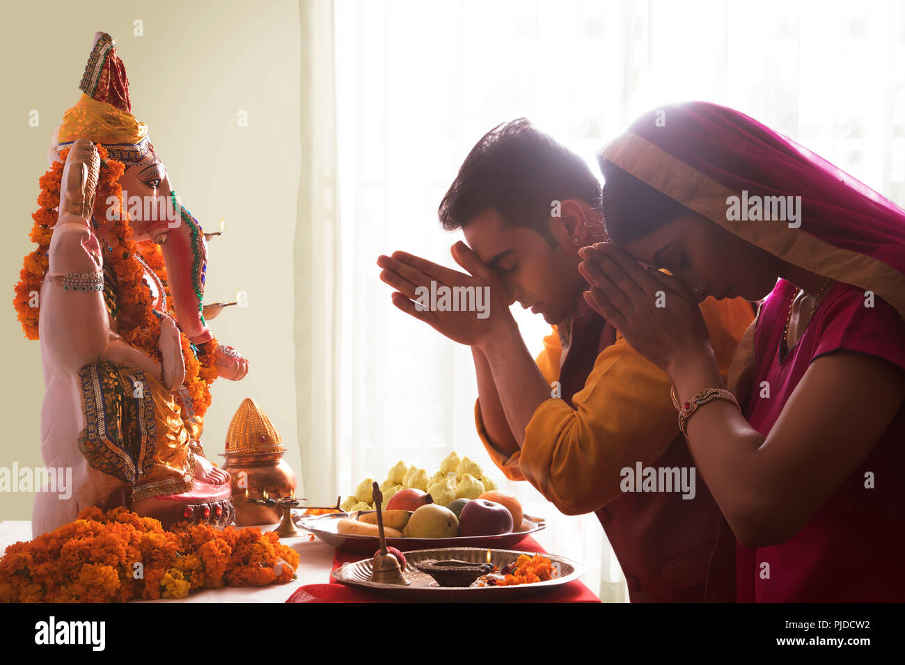 El esposo y la esposa rezando con las manos juntas en frente de Ganesha Idol en ocasión de Ganesh Chaturthi Foto de stock
