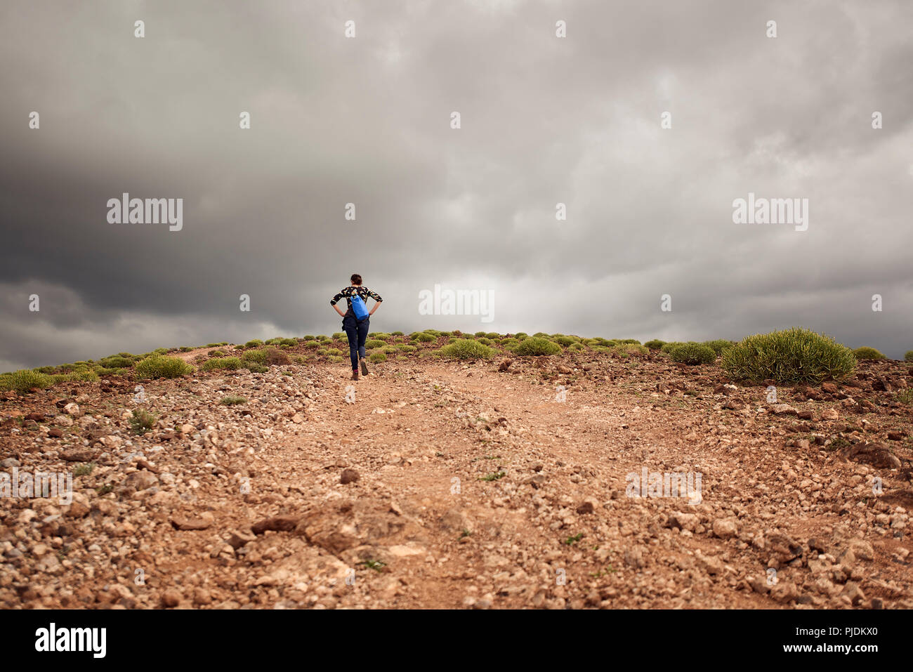 Mujer caminata cuesta arriba en pista de tierra, vista trasera, Las Palmas, Gran Canaria, Islas Canarias, España Foto de stock